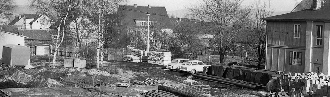 Baustelle in einem Wohngebiet um 1970: Steine und Rohre, Stahlstangen, verschiedenes Baumaterial, ein Trabi und ein Lada in einem Wohnviertel